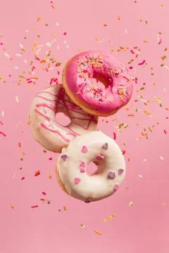 Various decorated doughnuts in motion falling on pink background. Stock Photos