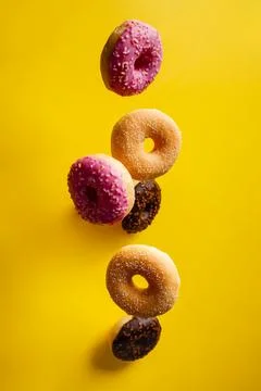 Various decorated doughnuts in motion falling on yelloy background Foto stock