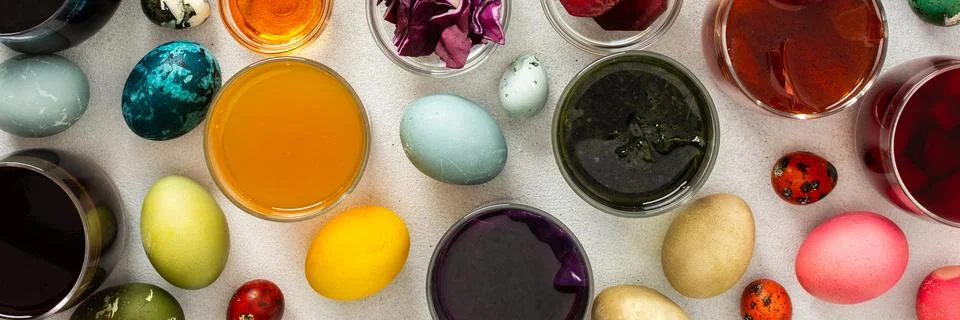 Various dyed Easter eggs in different colors are surrounded by bowls of natur Stock Photos