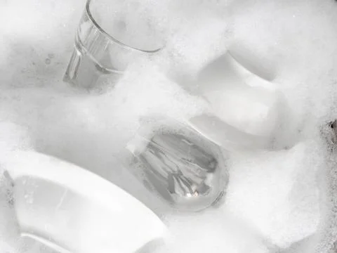 Various earthenware and glassware in soapy foam in sink with soapy water Stock Photos