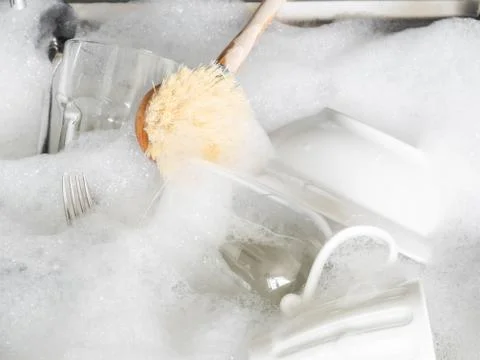 Various earthenware and glassware in soapy foam and wood brush in sink with s Stock Photos