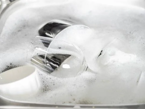 Various earthenware and glassware in soapy foam in a sink with soapy water Stock Photos