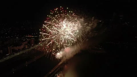 Various fireworks explode over the river near the city at night, shot with drone 스톡 동영상 165341492