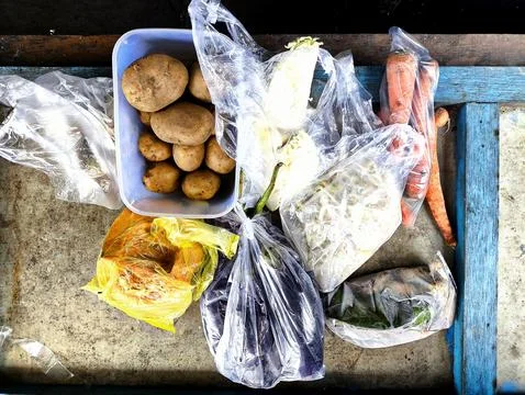 Various fresh vegetables wrapped in transparent plastic bags on wooden table. Stock Photos