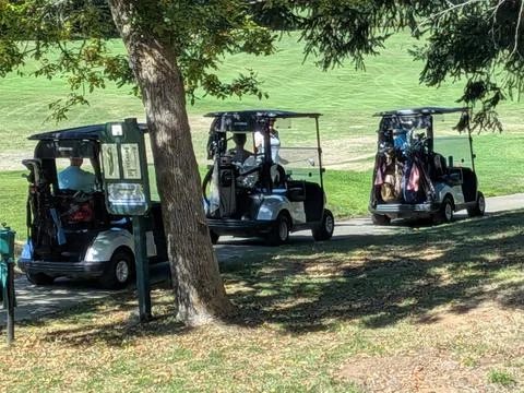 Various golf carts lined on cement path with players and golf bags Stock Photos