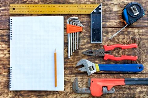 Various hand tools and blank notepad with pencil on old wooden background. Stock Photos