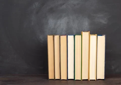 Various hardback books on the background of an empty black chalk board Stock Photos