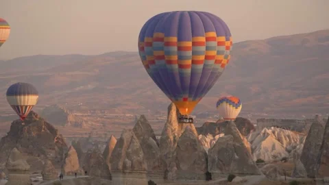 Various hot air balloons of different colours fly over cliff Stock Footage 149645282