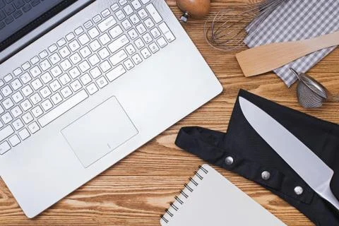 Various kitchenware utensils and laptop the wooden background, top view. Stock Photos