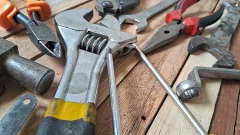 Various metallic construction tools arranged on a rustic wooden table surface Stock Photos