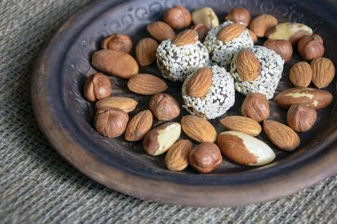 Various nuts in brown handmade clay plate on gray burlap Stock-Fotos