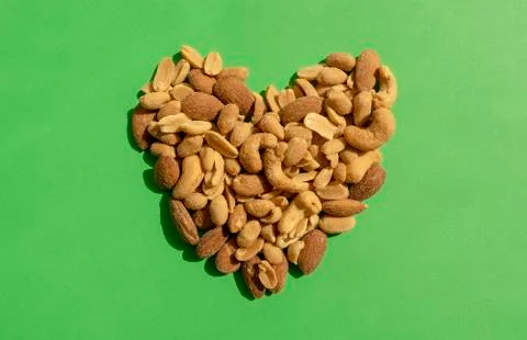 Various nuts forming heart shape on green background. Top view. Stock Photos