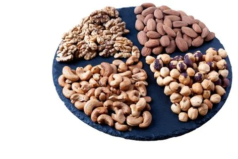 Various nuts sorted on black stone plate isolated on white background. Round Stock Photos