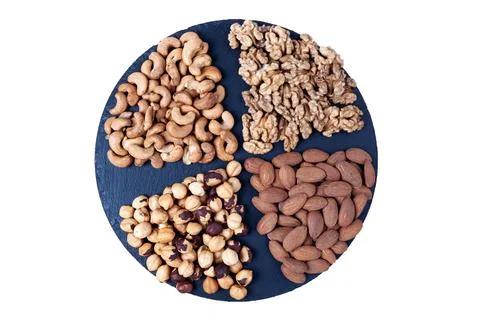 Various nuts sorted on black stone plate isolated on white background. Round Stock Photos