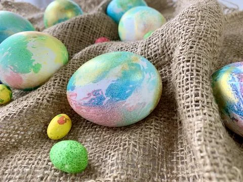 Various pastel-colored Easter eggs are arranged on textured burlap fabric, Stock Photos