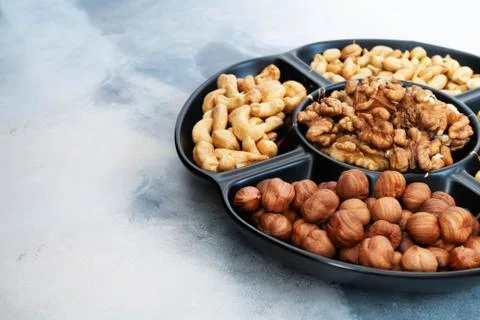 Various peeled nuts (hazelnuts, cashews, walnuts, peanuts) in a black bowl Stock Photos