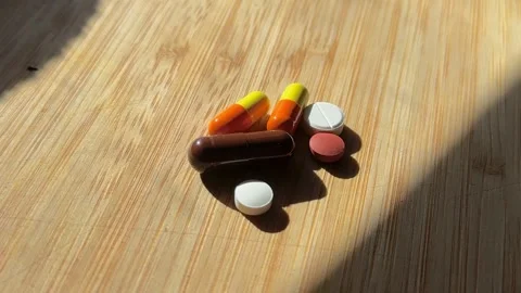 Various pills and capsules lying on a wooden surface in daylight Stock Footage 305830960
