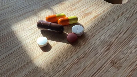 Various pills and capsules lying on a wooden surface in daylight Stock Footage 305830991
