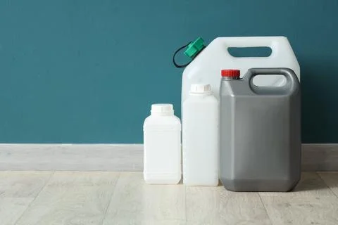 Various plastic containers and jerrycans lined up on floor against teal wall Stock Photos
