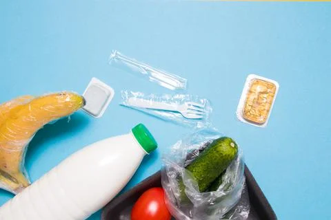 Various plastic packaging on a blue background, a tray with tomatoes and cucu Stock Photos
