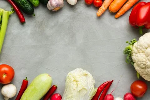 Various raw vegetables on a gray background with copy space in center. Stock Photos
