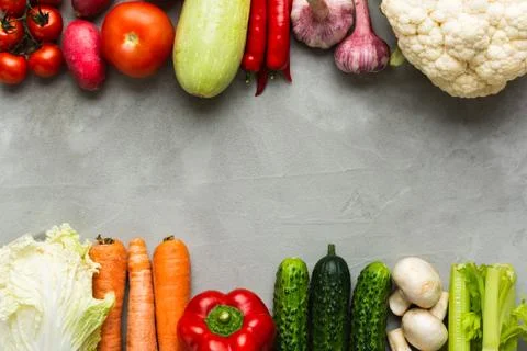 Various raw vegetables on a gray background with copy space in the center. Zu Stock Photos