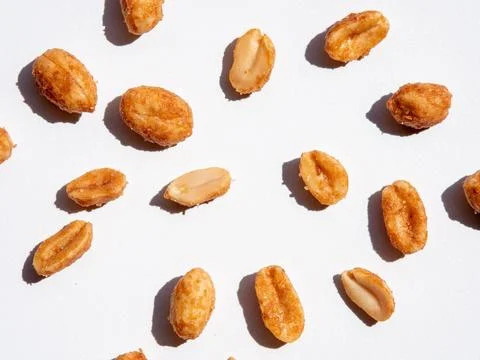 Various roasted peanuts are scattered on white surface, showcasing their te.. Stock Photos