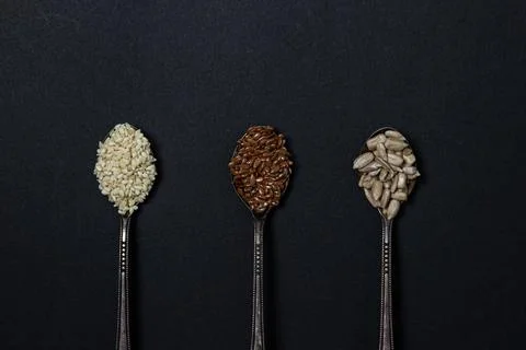 Various seeds on a black background. Three spoons with flax seeds, sesame seeds  Stock Photos