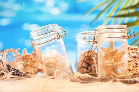 Various shells and starfish in jars on the azure seashore. Stock Photos