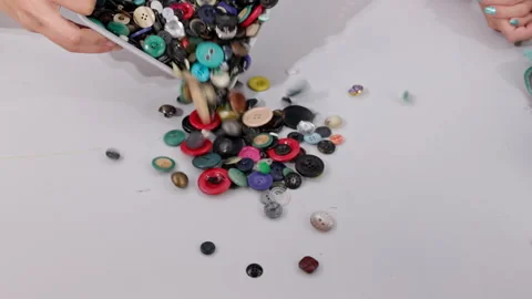 Various sizes and colors of buttons are dumped from a plastic container on the Stock Footage 241067140