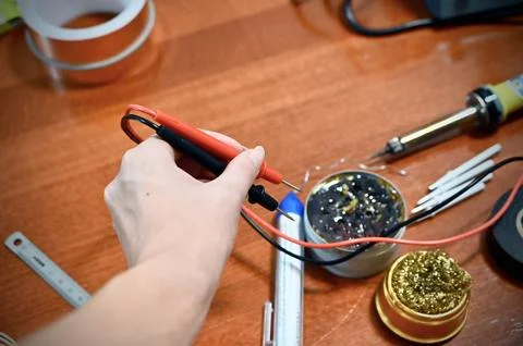 Various soldering and electronics tools on a table with a womans hand holding Fotos de archivo