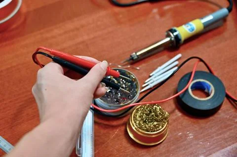 Various soldering and electronics tools on a table with a womans hand holding Fotos de archivo