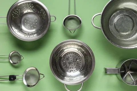Various stainless steel kitchen strainers on green background Stock Photos