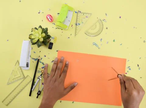 Various study materials scattered on a yellow paper background while a person Stock Photos