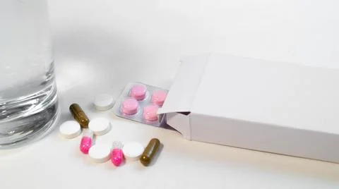Various tablets are scattered and in a box next to a glass of water Stock Photos