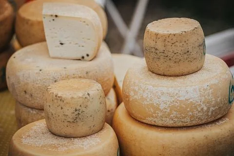 Various types of cheese displayed at a market, including round and square s.. Stock Photos