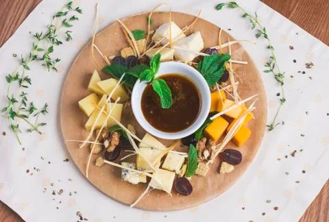 Various types of cheese sliced on round wooden board with grapes, honey and m Stock Photos