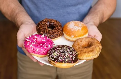 Various types of donuts on the plate closeup in male's hands. Stock Photos