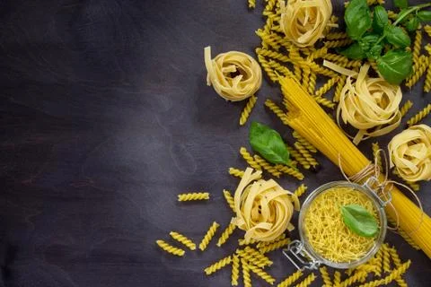 Various types of pasta with basil on a kitchen wooden table. Stock Photos