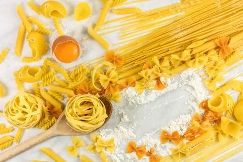 Various types of pasta on marble with egg and copyspace Stock Photos