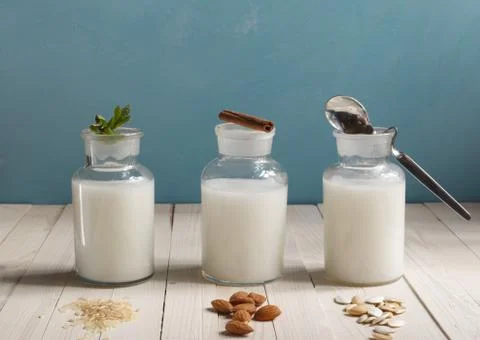 Various types of plant-based lactose-free milk in glass bottles on a blue Stock Photos