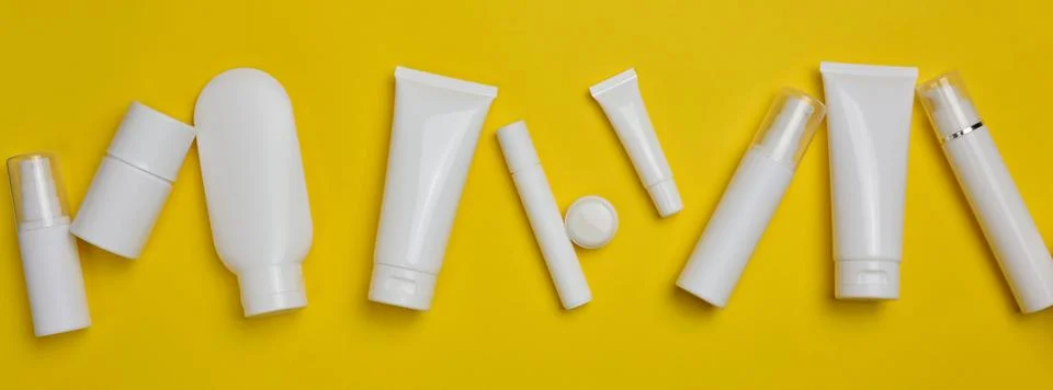 Various types of white plastic packaging: a bottle, a jar, a tube on a yell.. Stock Photos