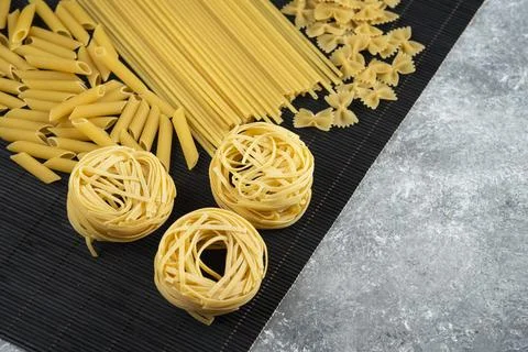 Various uncooked pasta on black bamboo sheet Stock Photos