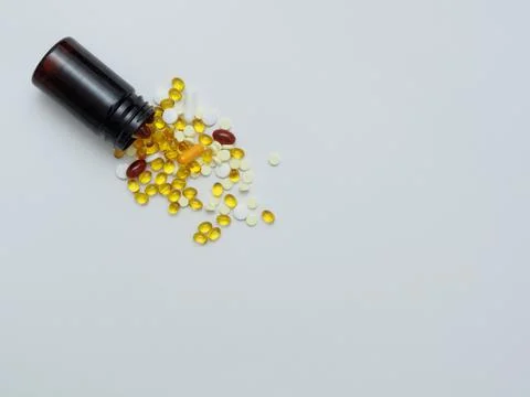 Various vitamins D, E, C fish oil in a dark plastic jar sprinkled on a white Stock Photos