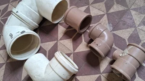 Various white and brown plastic plumbing pipes on tiled floor Stock Photos