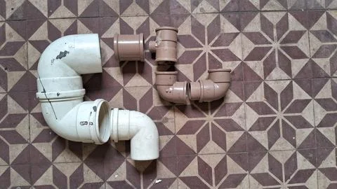 Various white and brown plastic pipe fittings arranged on floor tiles Stock Photos