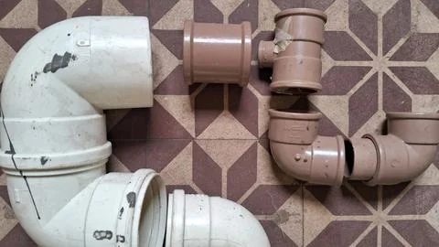 Various white and brown plastic plumbing pipes arranged on tiled floor Stock Photos
