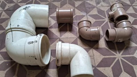 Various white and brown plastic pipe fittings arranged on floor Stock Photos