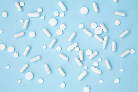 Various white medication tablets and capsules on blue background. Concept of  Stock Photos