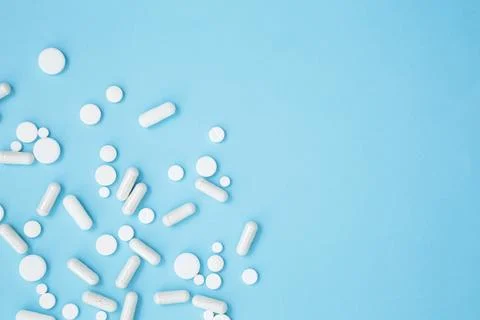Various white medication tablets and capsules on blue background. Concept of  Stock Photos